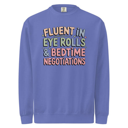 Blue sweatshirt with colorful text 'Fluent in Eye Rolls & Bedtime Negotiations' on a white background