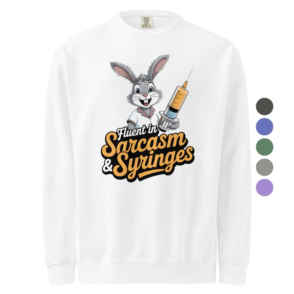 White long-sleeve shirt with cartoon character and text 'Fluent in Sarcasm & Syringes' on a white background.