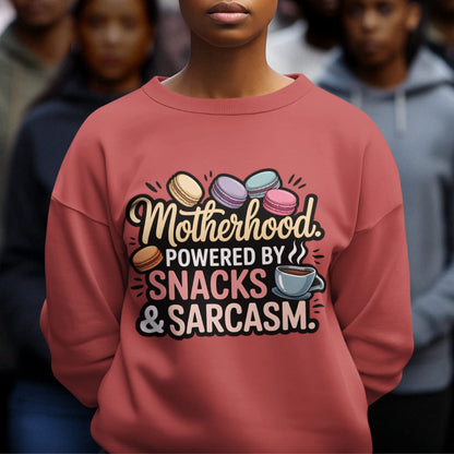 Sweatshirt design with text “Motherhood. Powered by Snacks & Sarcasm.” featuring colorful macarons and a steaming coffee cup on vintage-washed cotton fleece.