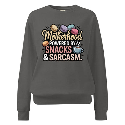 Sweatshirt design with text “Motherhood. Powered by Snacks & Sarcasm.” featuring colorful macarons and a steaming coffee cup on vintage-washed cotton fleece.
