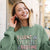 Woman wearing a green sweatshirt with text, listening to music with earphones outdoors.