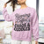 Person wearing a pink sweatshirt with text 'Running on Coffee, Chaos & Cuddles' in a casual setting.