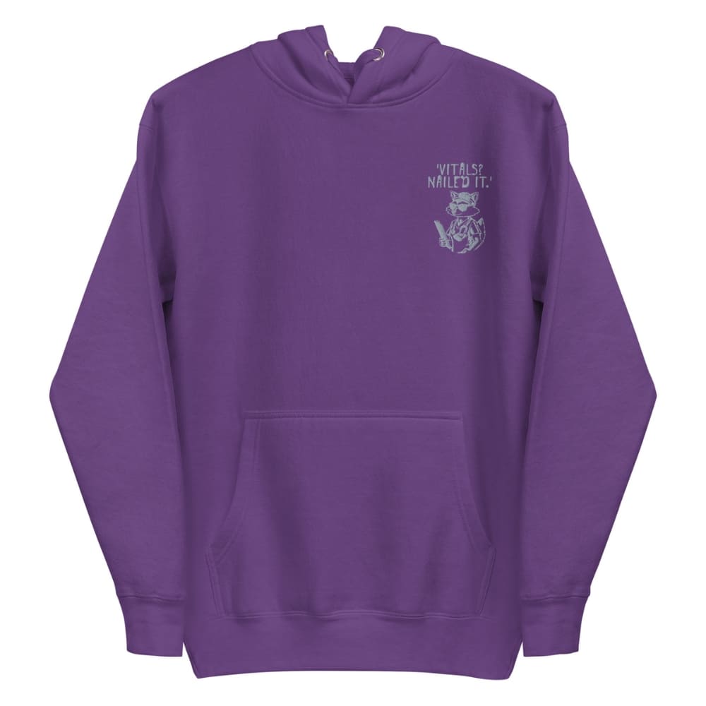 Raccoon nurse graphic wearing scrubs and sunglasses holding a clipboard under the quote “Vitals? Nailed It.” – printed on a black Cotton Heritage hoodie