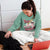 Woman wearing a green sweatshirt with a graphic design sitting on the floor with a laptop and a dog.
