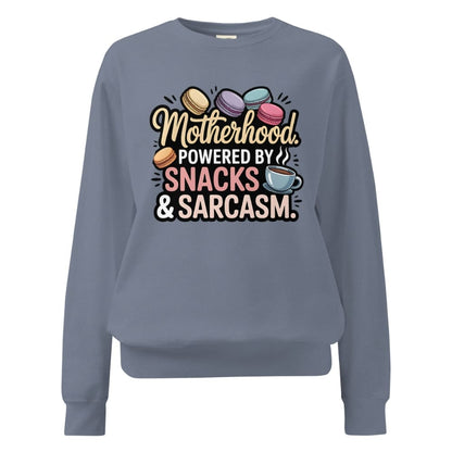 Sweatshirt design with text “Motherhood. Powered by Snacks & Sarcasm.” featuring colorful macarons and a steaming coffee cup on vintage-washed cotton fleece.