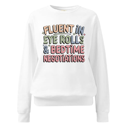 White sweatshirt with colorful text 'FLUENT IN EYE ROLLS & BEDTIME NEGOTIATIONS' on a white background