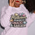 Sweatshirt design with text “Motherhood. Powered by Snacks & Sarcasm.” featuring colorful macarons and a steaming coffee cup on vintage-washed cotton fleece.