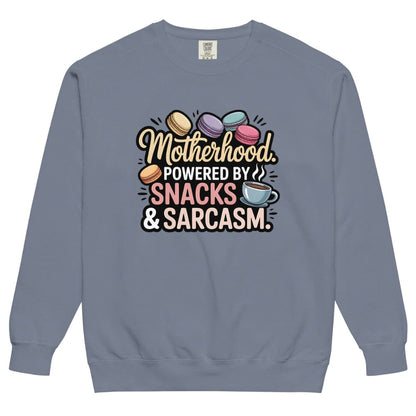 Sweatshirt design with text “Motherhood. Powered by Snacks & Sarcasm.” featuring colorful macarons and a steaming coffee cup on vintage-washed cotton fleece.