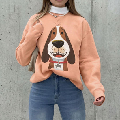 Person wearing a peach-colored sweatshirt with a dog graphic design against a concrete wall.