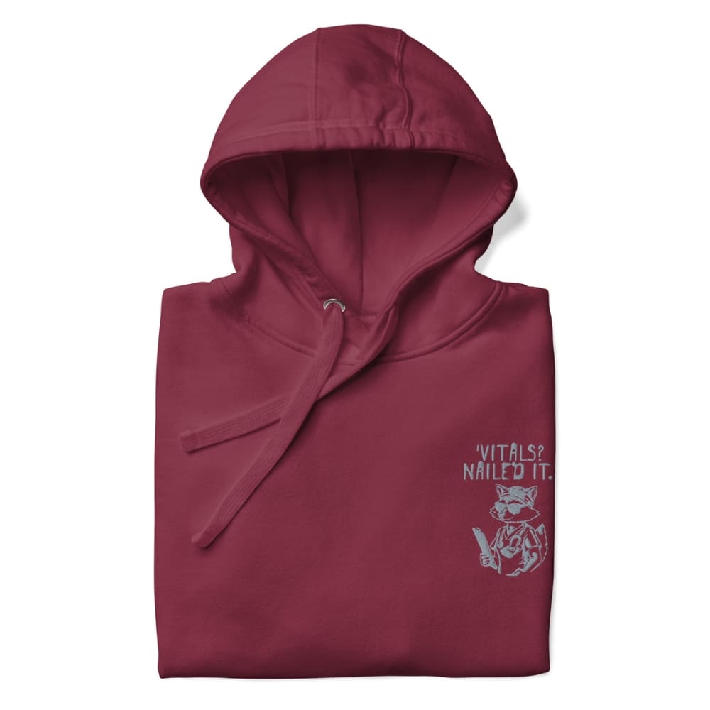 Raccoon nurse graphic wearing scrubs and sunglasses holding a clipboard under the quote “Vitals? Nailed It.” – printed on a black Cotton Heritage hoodie