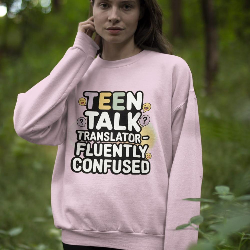 Person wearing a pink sweatshirt with text 'TEEN TALK TRANSLATOR - FLUENTLY CONFUSED' in a forest setting