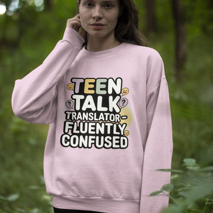 Person wearing a pink sweatshirt with text 'TEEN TALK TRANSLATOR - FLUENTLY CONFUSED' in a forest setting