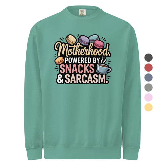 Sweatshirt design with text “Motherhood. Powered by Snacks & Sarcasm.” featuring colorful macarons and a steaming coffee cup on vintage-washed cotton fleece.