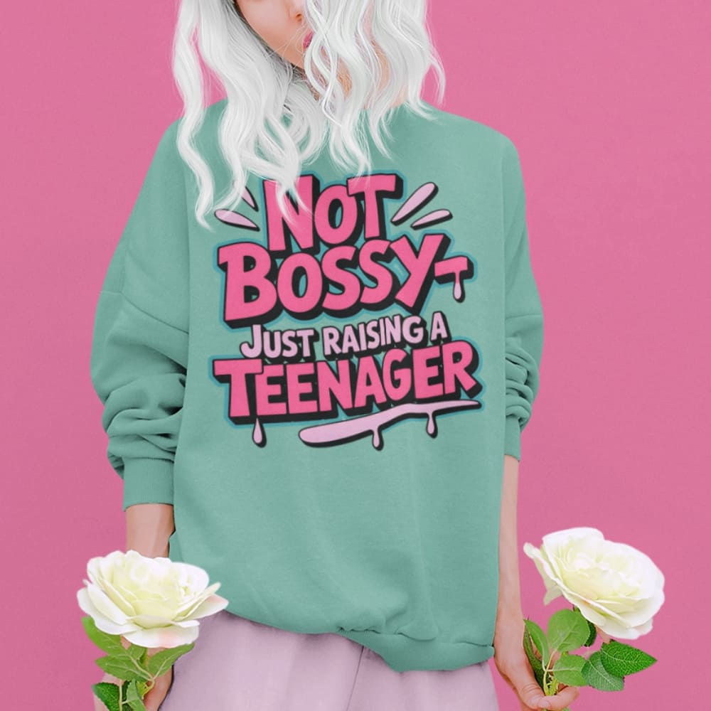 Person wearing a green sweatshirt with 'Not Bossy Just Raising a Teenager' text on a pink background