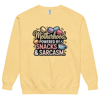Sweatshirt design with text “Motherhood. Powered by Snacks & Sarcasm.” featuring colorful macarons and a steaming coffee cup on vintage-washed cotton fleece.