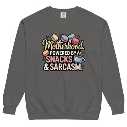 Sweatshirt design with text “Motherhood. Powered by Snacks & Sarcasm.” featuring colorful macarons and a steaming coffee cup on vintage-washed cotton fleece.