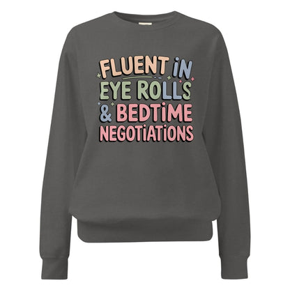 Gray sweatshirt with colorful text 'FLUENT IN EYE ROLLS & BEDTIME NEGOTIATIONS' on a white background