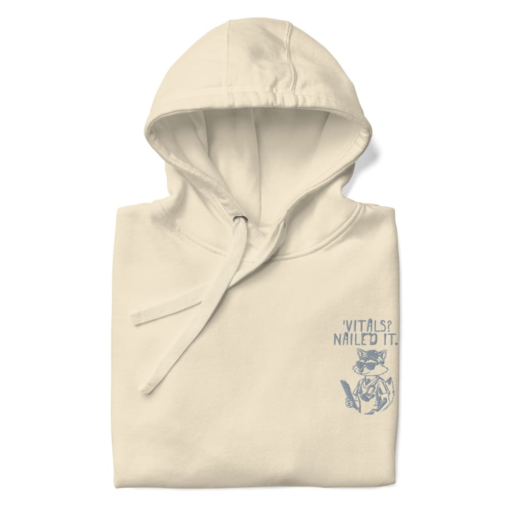 Raccoon nurse graphic wearing scrubs and sunglasses holding a clipboard under the quote “Vitals? Nailed It.” – printed on a black Cotton Heritage hoodie