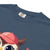 Cute cartoon owl cheerleader holding a pom-pom and clipboard, wearing a red cap with the quote “Behind Every Great Swing Is a Loud Mom” – featured on garment-dyed heavyweight cotton tee