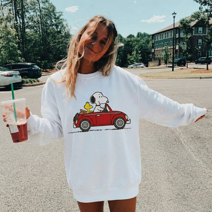 Woman wearing a white sweatshirt with a cartoon design, holding a drink, outdoors.