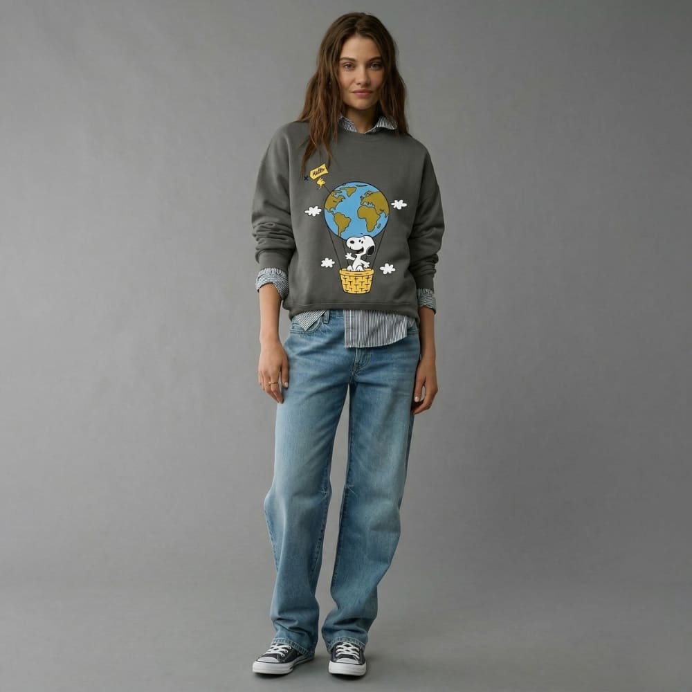 Person wearing a gray sweatshirt with a graphic design and blue jeans on a gray background
