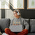 Person sitting on a couch with a laptop wearing a 'Coffee Fueled' sweatshirt, surrounded by framed plant art.