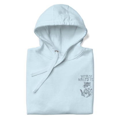 Raccoon nurse graphic wearing scrubs and sunglasses holding a clipboard under the quote “Vitals? Nailed It.” – printed on a black Cotton Heritage hoodie