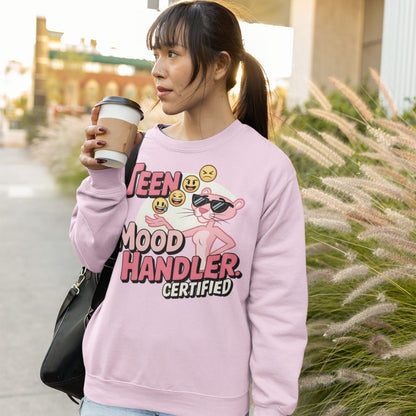 Person wearing a pink sweatshirt with graphic design and text, holding a coffee cup outdoors.