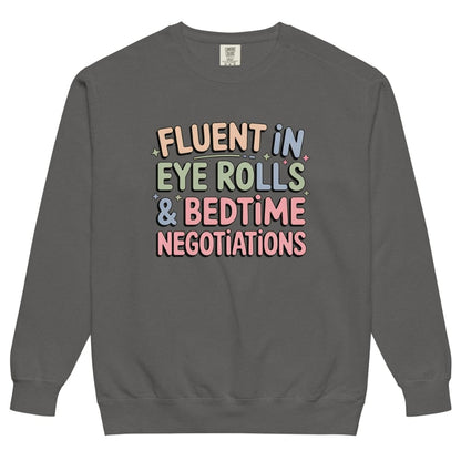 Gray sweatshirt with colorful text 'Fluent in Eye Rolls & Bedtime Negotiations' on a white background