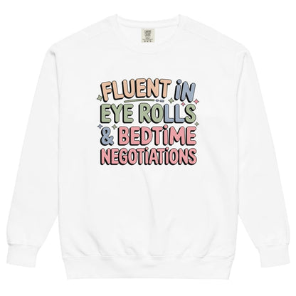 White sweatshirt with colorful text 'Fluent in Eye Rolls & Bedtime Negotiations' on a white background
