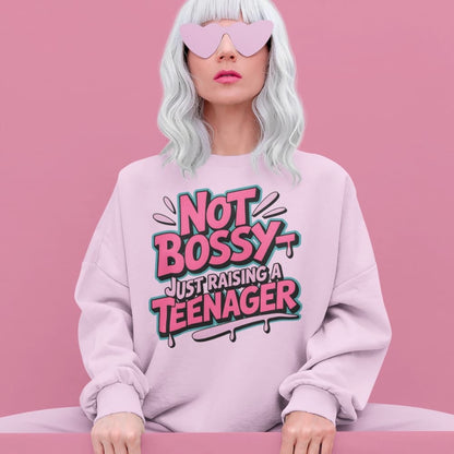 Person wearing a pink sweatshirt with 'Not Bossy Just Raising a Teenager' text on a pink background