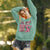 Woman wearing a teal hoodie with a pink Panther graphic and 'Cool Mom Club' text, standing outdoors.