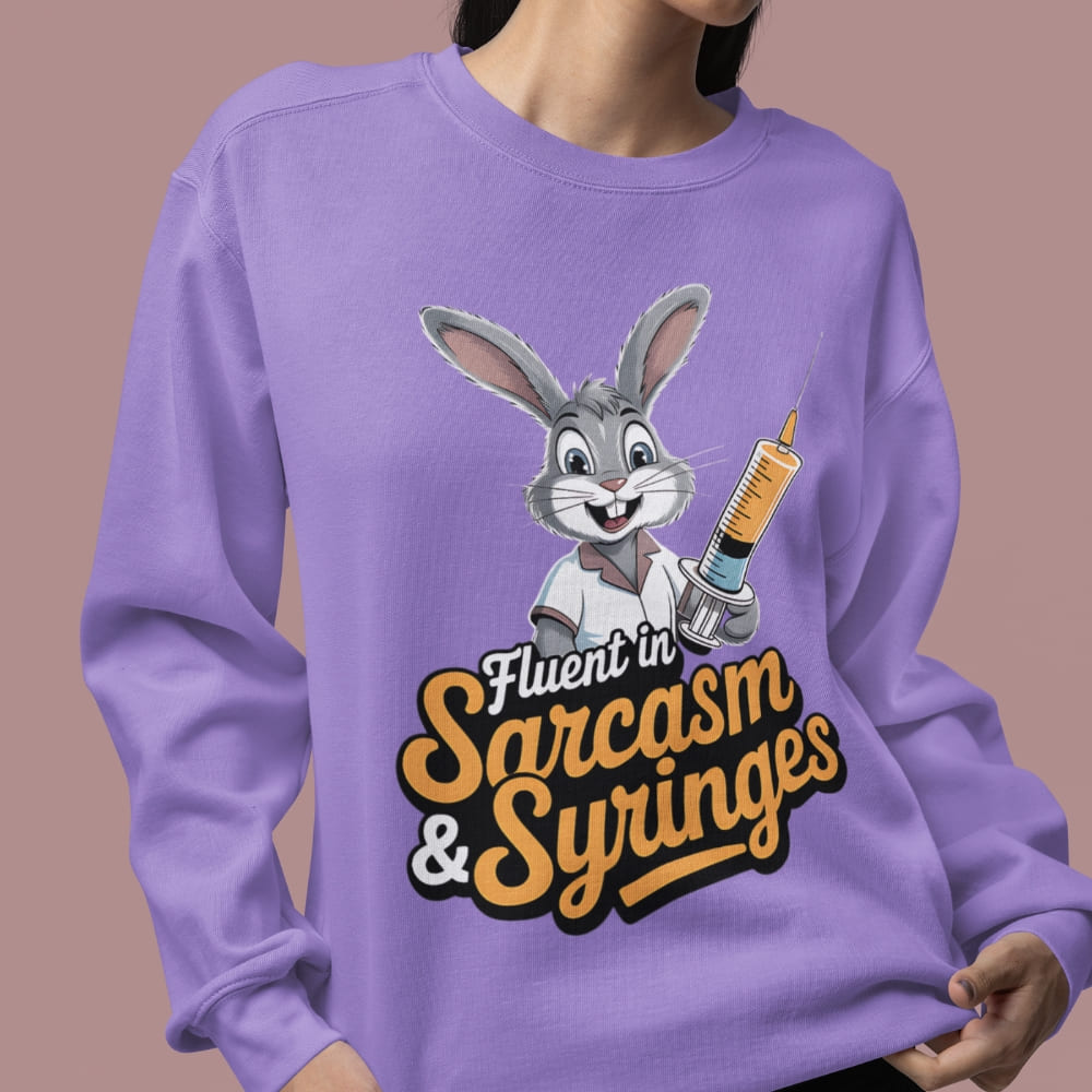 Person wearing a purple sweatshirt with a cartoon character and text 'Fluent in Sarcasm & Syringes' on a brown background