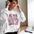 Person wearing a white sweatshirt with a pink Panther design and text, sitting at a desk with a laptop.