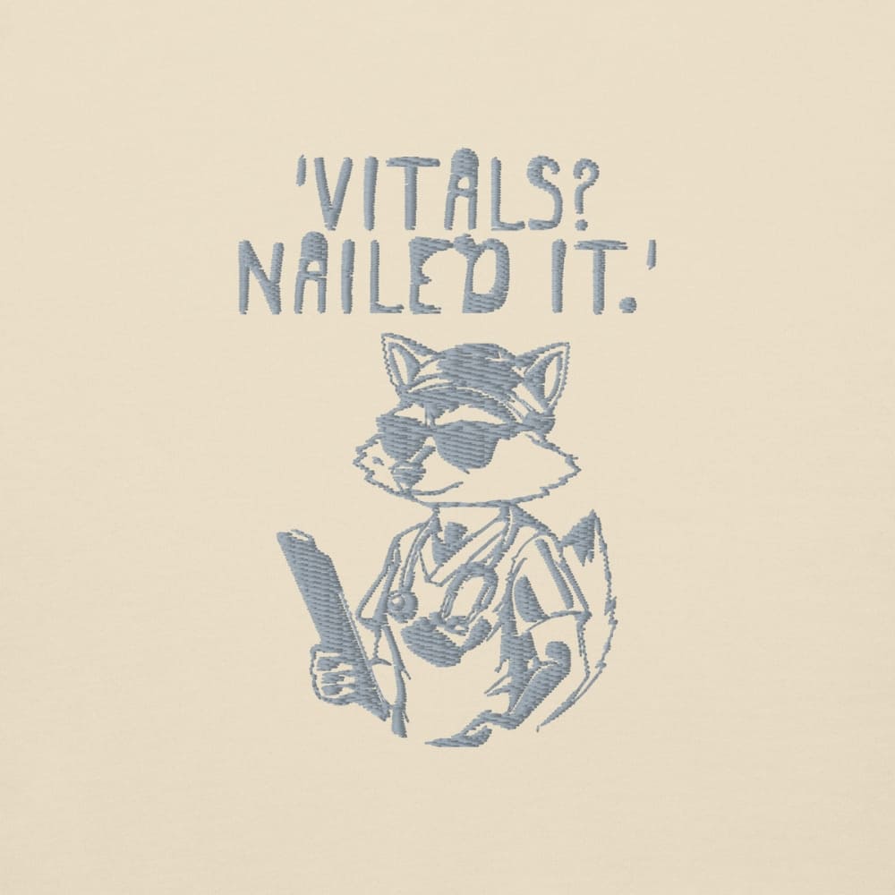 Raccoon nurse graphic wearing scrubs and sunglasses holding a clipboard under the quote “Vitals? Nailed It.” – printed on a black Cotton Heritage hoodie