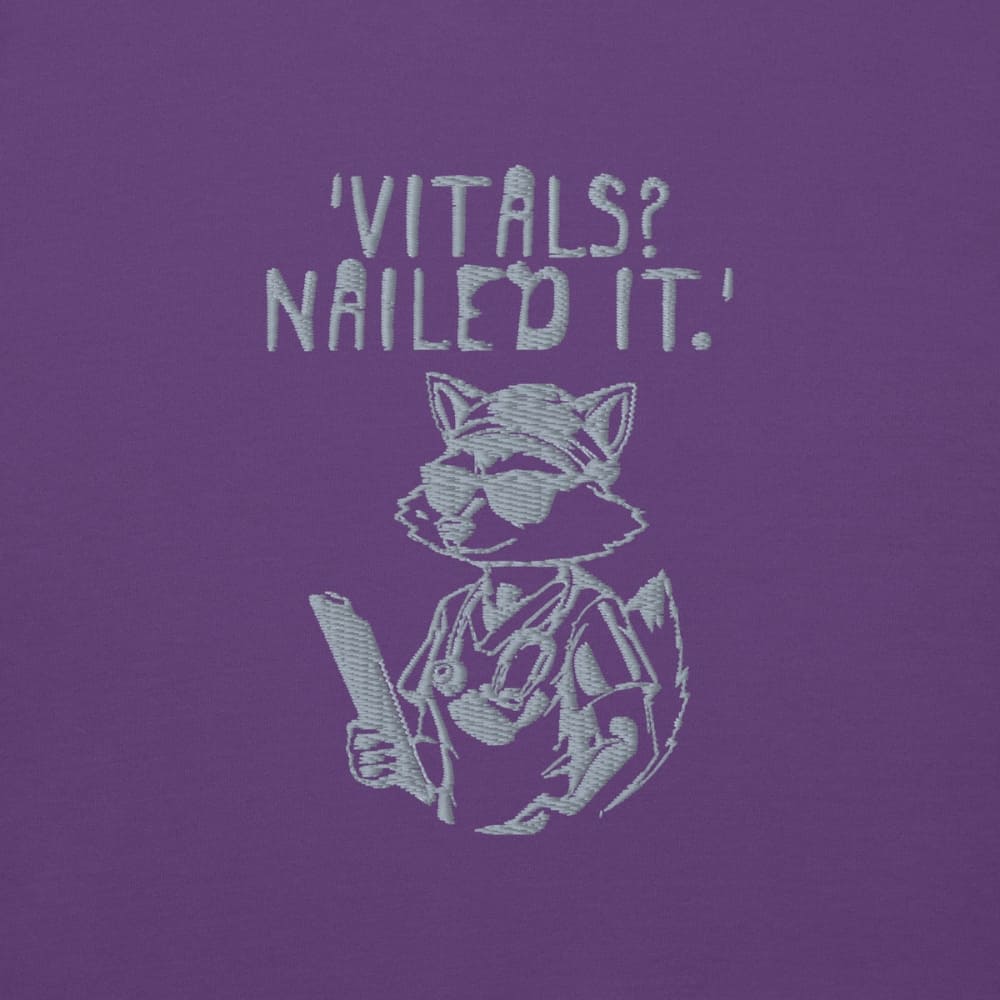 Raccoon nurse graphic wearing scrubs and sunglasses holding a clipboard under the quote “Vitals? Nailed It.” – printed on a black Cotton Heritage hoodie