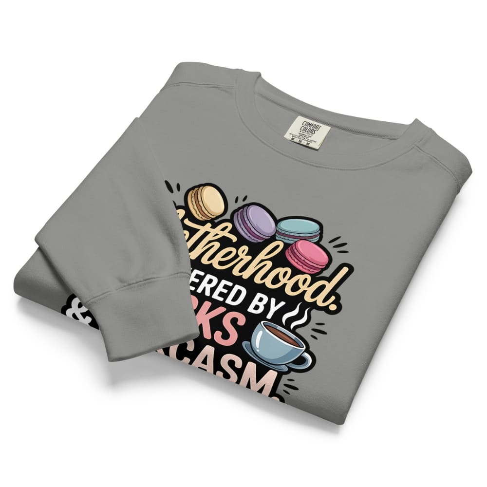 Sweatshirt design with text “Motherhood. Powered by Snacks & Sarcasm.” featuring colorful macarons and a steaming coffee cup on vintage-washed cotton fleece.