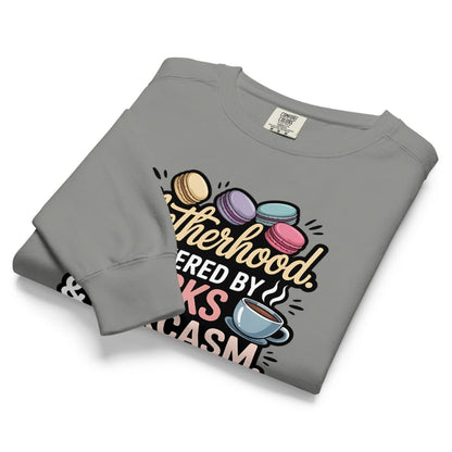Sweatshirt design with text “Motherhood. Powered by Snacks & Sarcasm.” featuring colorful macarons and a steaming coffee cup on vintage-washed cotton fleece.