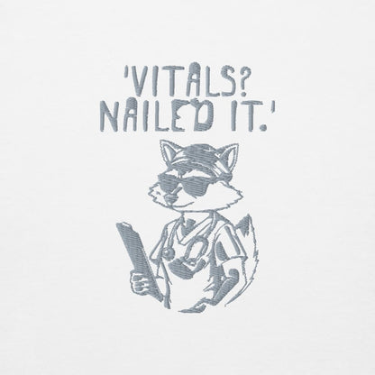 Raccoon nurse graphic wearing scrubs and sunglasses holding a clipboard under the quote “Vitals? Nailed It.” – printed on a black Cotton Heritage hoodie