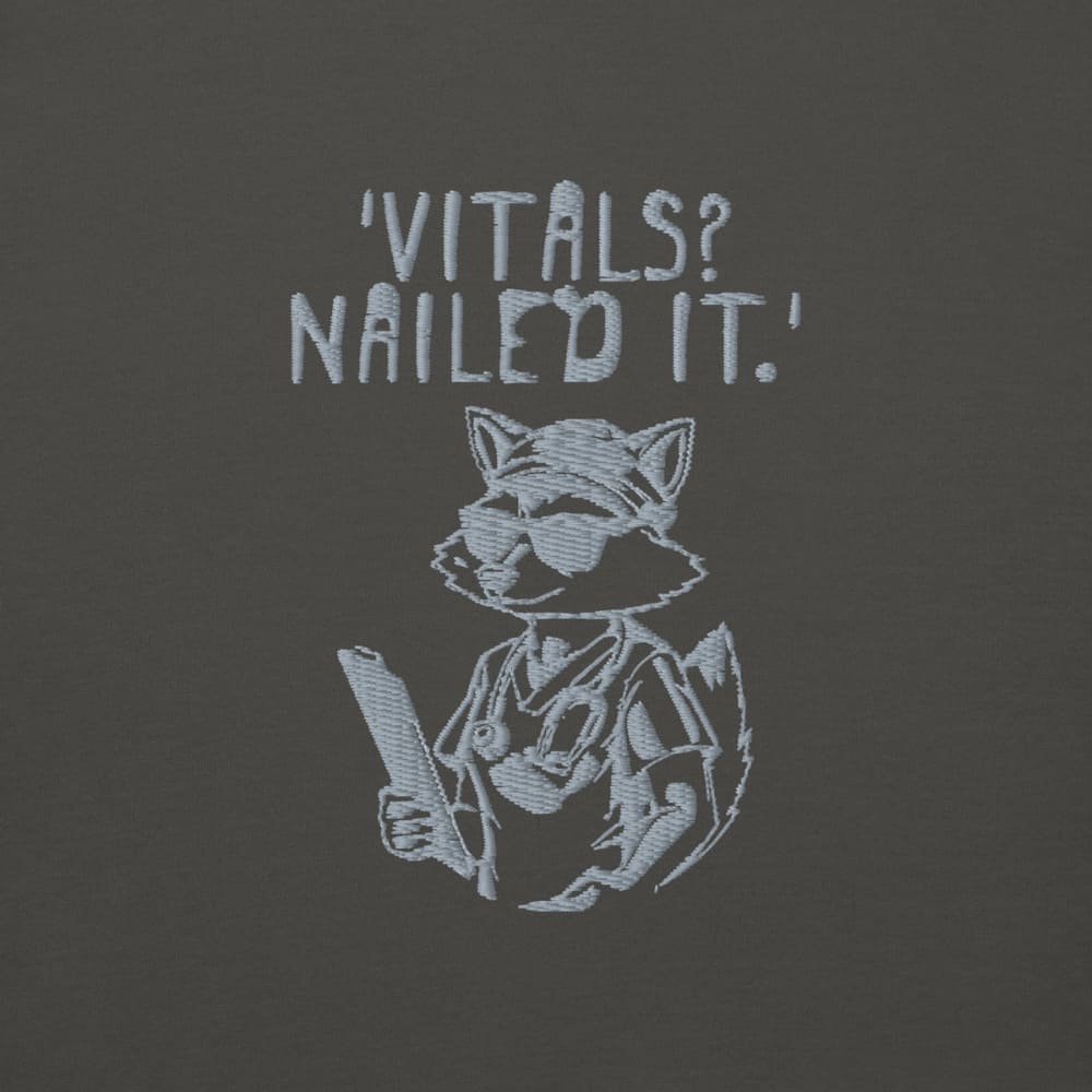 Raccoon nurse graphic wearing scrubs and sunglasses holding a clipboard under the quote “Vitals? Nailed It.” – printed on a black Cotton Heritage hoodie