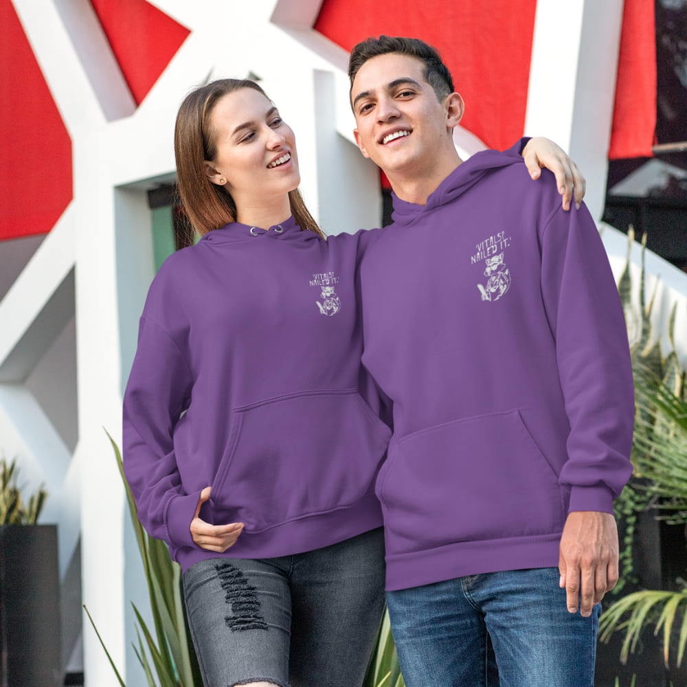 Raccoon nurse graphic wearing scrubs and sunglasses holding a clipboard under the quote “Vitals? Nailed It.” – printed on a black Cotton Heritage hoodie