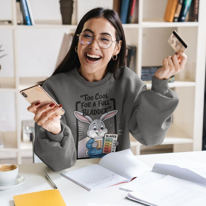 Woman wearing a sweatshirt with a graphic design, holding a phone and a credit card, in an office setting.