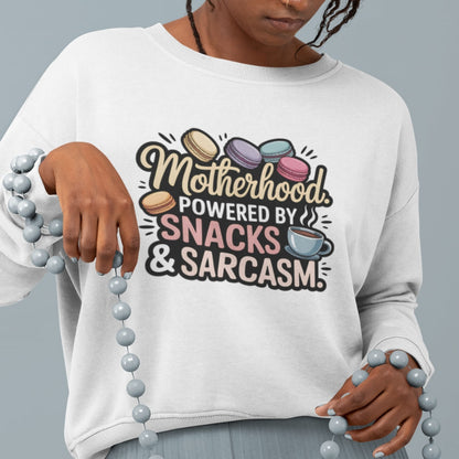 Sweatshirt design with text “Motherhood. Powered by Snacks & Sarcasm.” featuring colorful macarons and a steaming coffee cup on vintage-washed cotton fleece.
