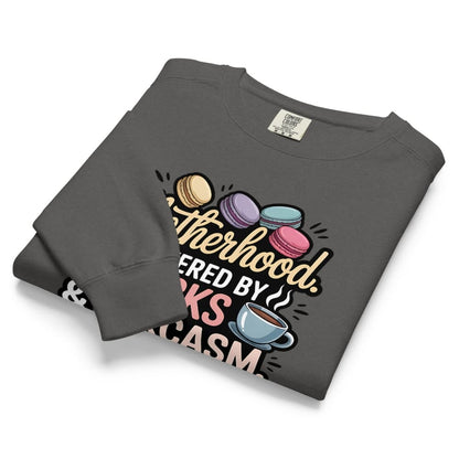 Sweatshirt design with text “Motherhood. Powered by Snacks & Sarcasm.” featuring colorful macarons and a steaming coffee cup on vintage-washed cotton fleece.
