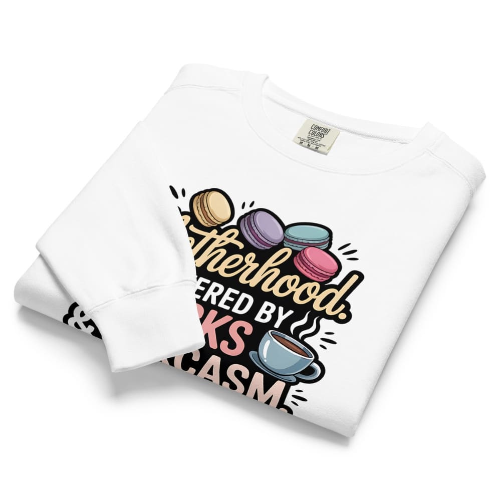 Sweatshirt design with text “Motherhood. Powered by Snacks & Sarcasm.” featuring colorful macarons and a steaming coffee cup on vintage-washed cotton fleece.