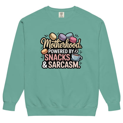 Sweatshirt design with text “Motherhood. Powered by Snacks & Sarcasm.” featuring colorful macarons and a steaming coffee cup on vintage-washed cotton fleece.