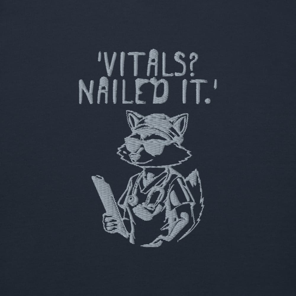 Raccoon nurse graphic wearing scrubs and sunglasses holding a clipboard under the quote “Vitals? Nailed It.” – printed on a black Cotton Heritage hoodie