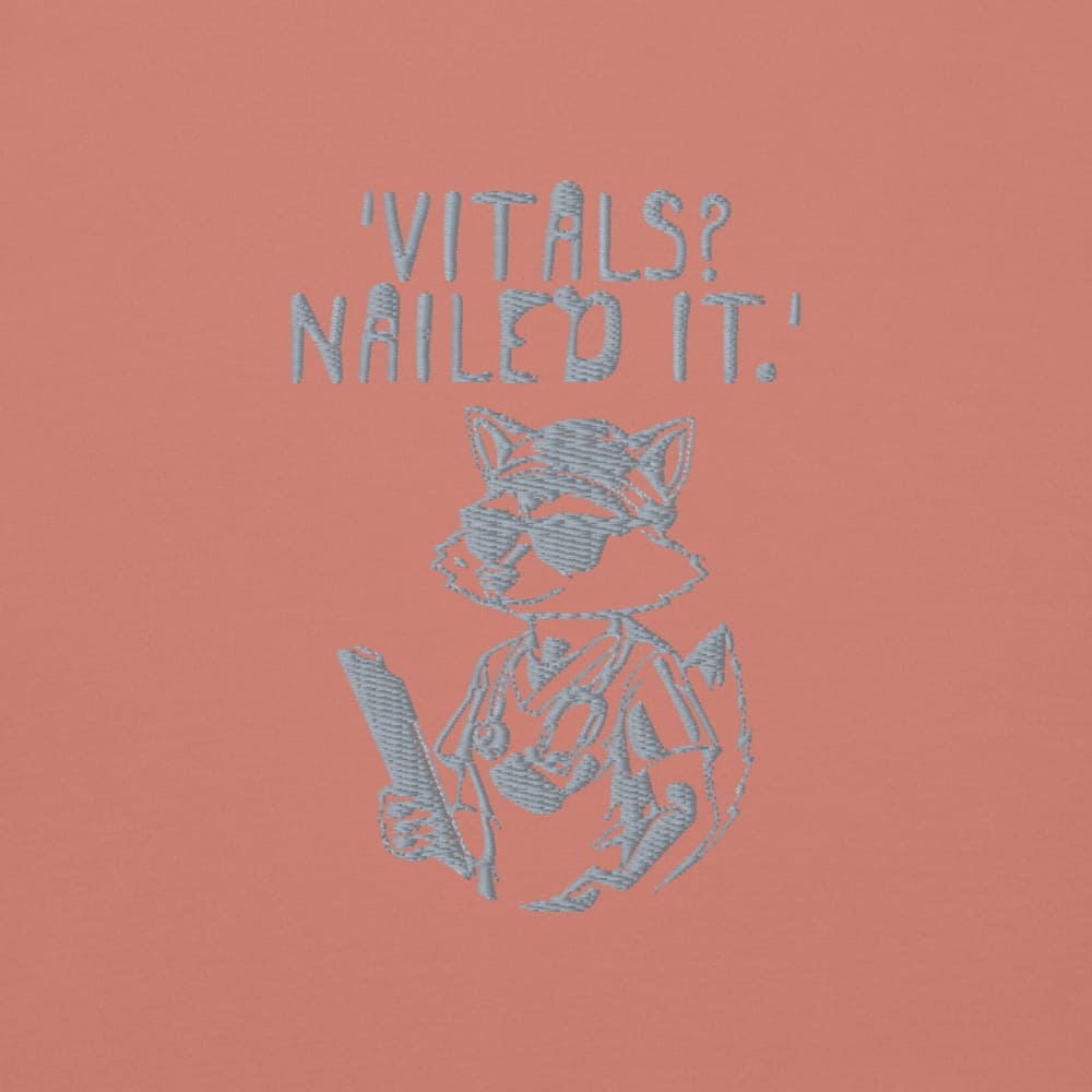 Raccoon nurse graphic wearing scrubs and sunglasses holding a clipboard under the quote “Vitals? Nailed It.” – printed on a black Cotton Heritage hoodie