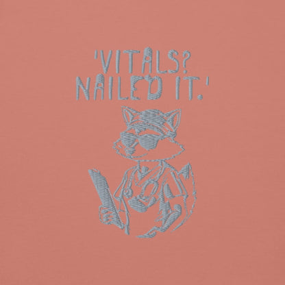 Raccoon nurse graphic wearing scrubs and sunglasses holding a clipboard under the quote “Vitals? Nailed It.” – printed on a black Cotton Heritage hoodie
