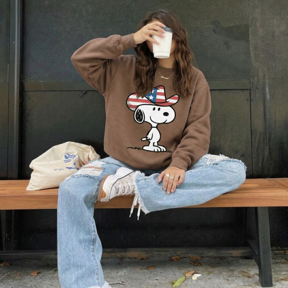 Person wearing a brown sweatshirt with a cartoon character sitting on a bench.